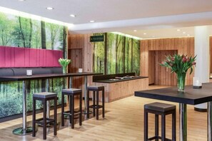 Un espace bar moderne avec un comptoir en bois, des tabourets de bar et un coin salon agrémenté d’un banc rouge.