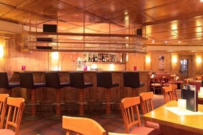Eine Bar mit Holzbarhocker, einer Theke mit Flaschen und einer Sitzecke mit Tischen und Stühlen.