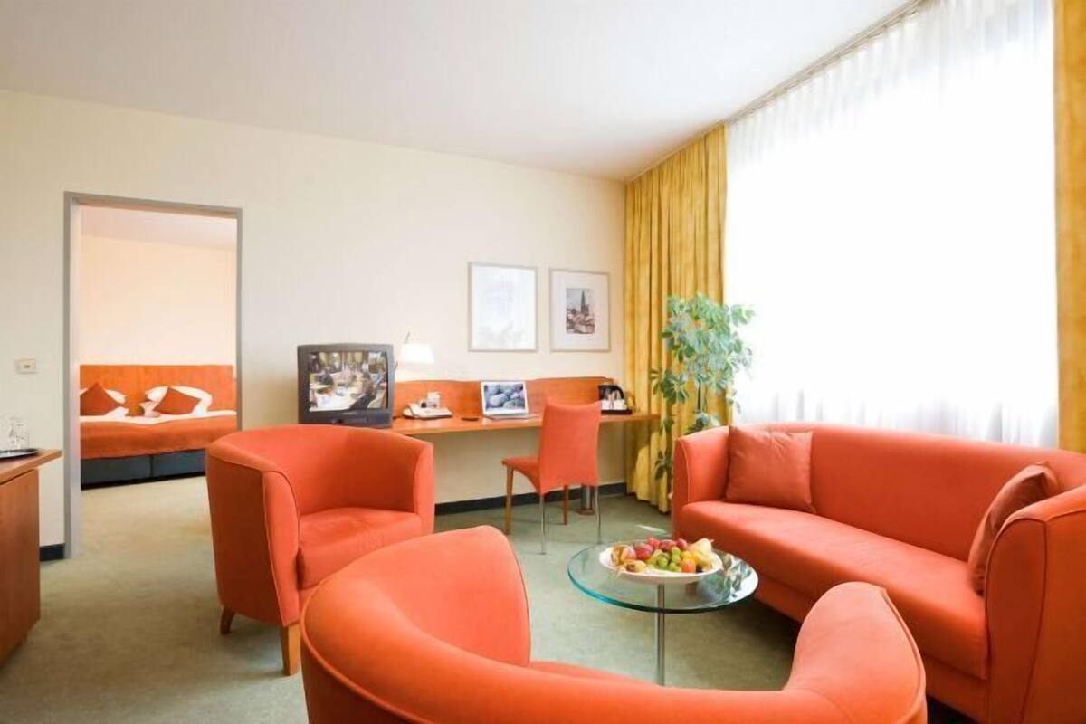 A hotel room with orange furniture, a desk, a chair, a bed, and a window with curtains.