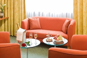 Una habitación con un sofá rojo, dos mesas redondas con bebidas y aperitivos, y una botella de champán.