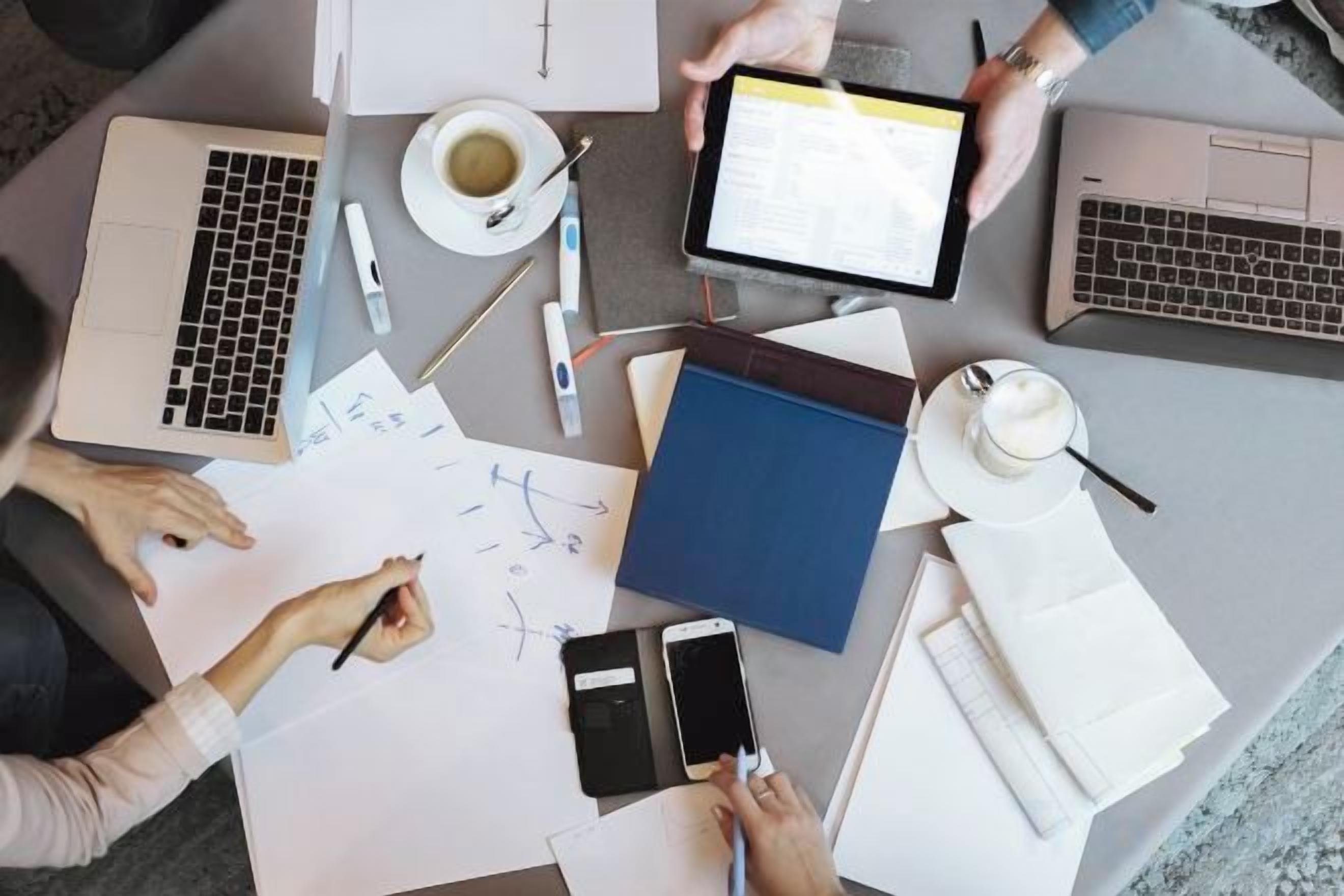 A workspace with laptops, papers, a smartphone, and a coffee cup.