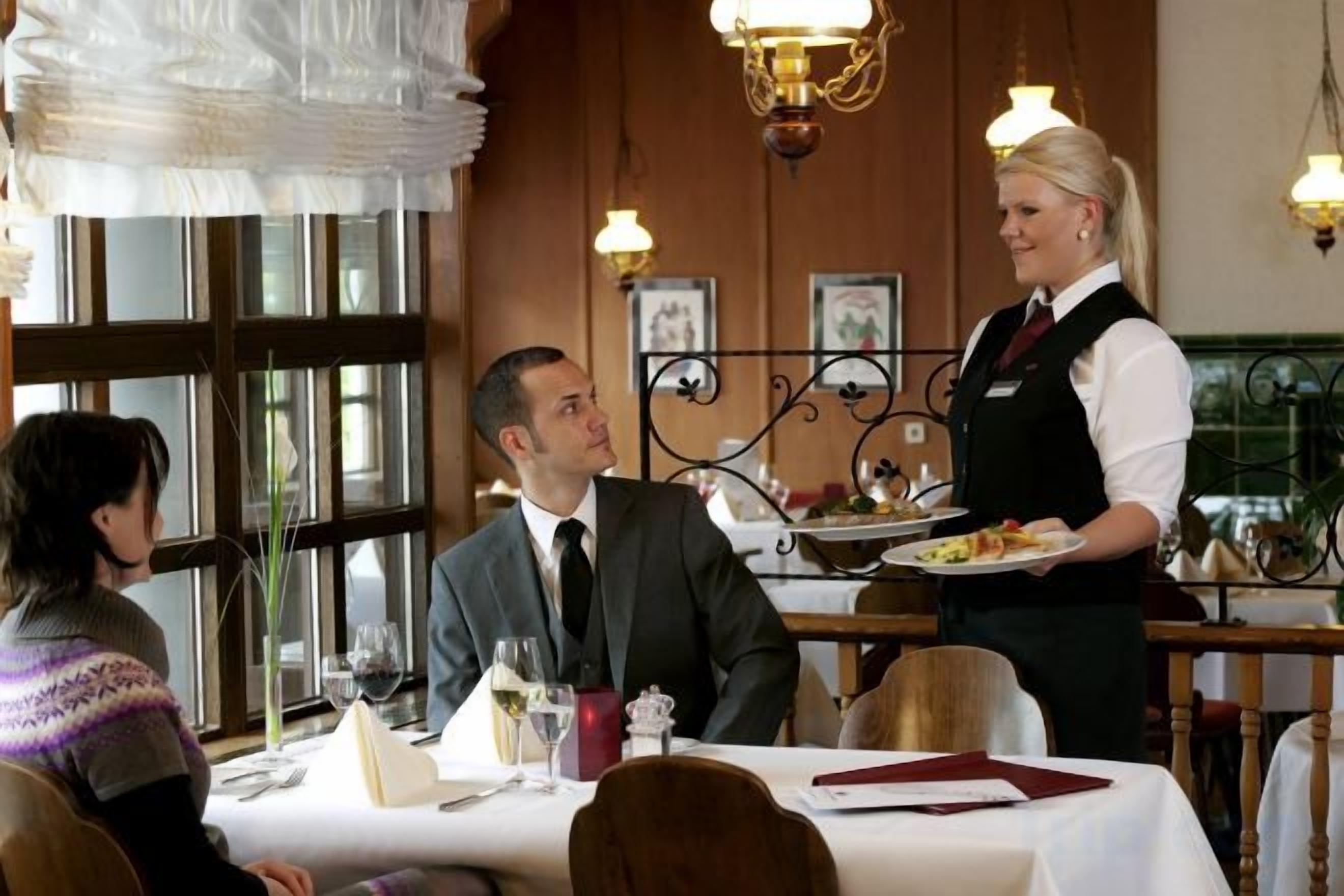 Interior de un restaurante con un camarero sirviendo un plato a una pareja sentada.