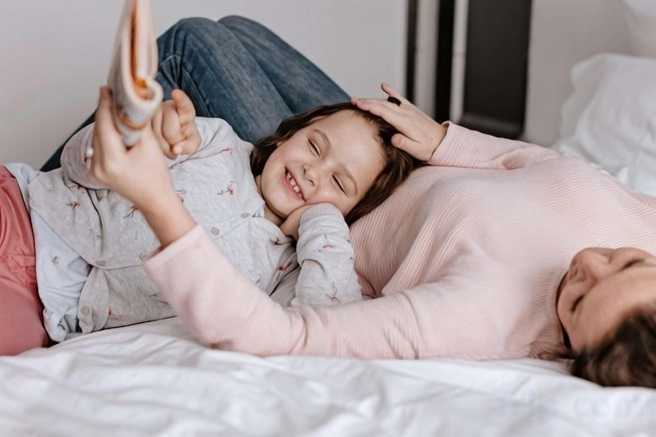 En person ligger på en säng och läser en bok, och har pyjamas på sig.