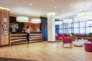A reception area with a wooden reception desk, multiple seating options, and large pendant lights. - Mercure Hotel Offenburg am Messeplatz (Offenburg)