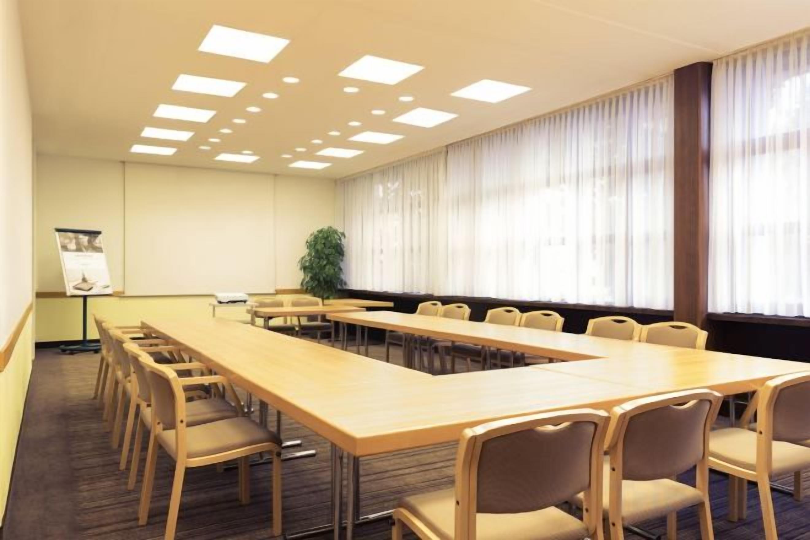 Une salle de conférence avec une longue table, des chaises, un écran de projection et une fenêtre avec des rideaux.