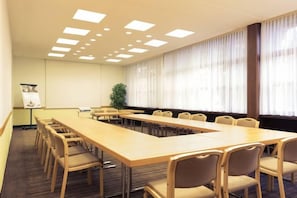 Una sala conferenze con un lungo tavolo, sedie, uno schermo per proiettore e una finestra con tende.