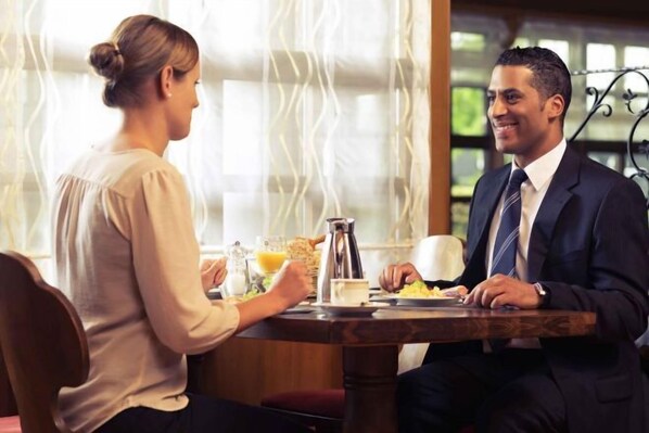 Una mesa de comedor con una cafetera, un vaso de zumo de naranja y platos de comida.
