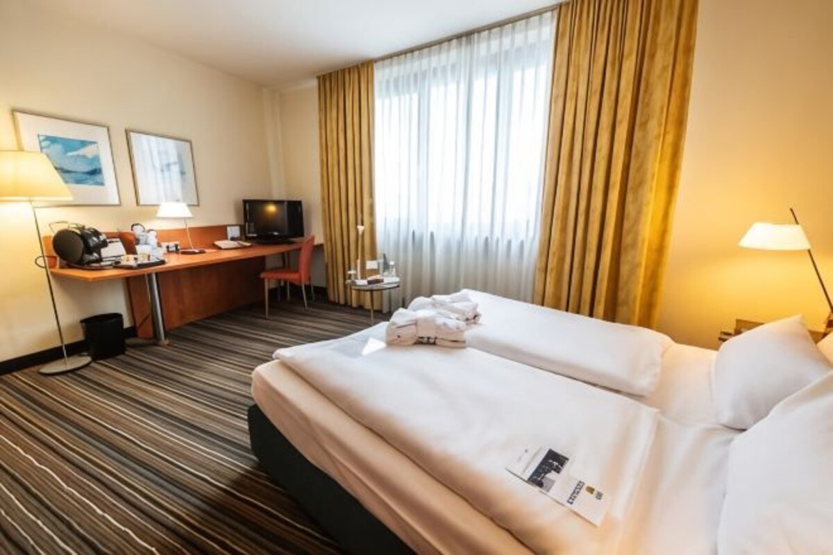 A hotel room with a bed, desk, chair, television, and curtains.