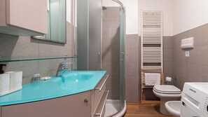 Ein Badezimmer mit Duschkabine aus Glas, einem Waschbecken mit Armatur, einer Toilette und einem Handtuchhalter.