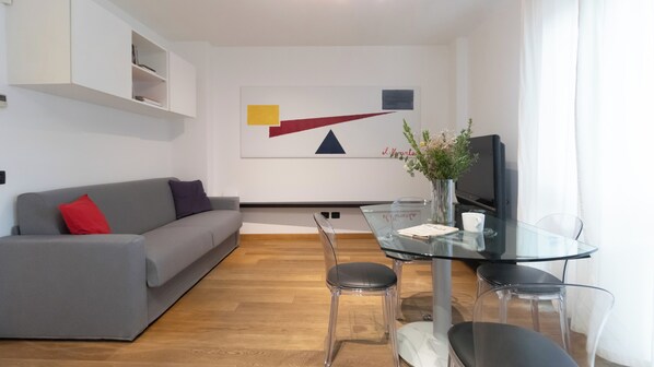 Ein modernes Wohnzimmer mit einem grauen Sofa, einem Glastisch und einem Fernseher.