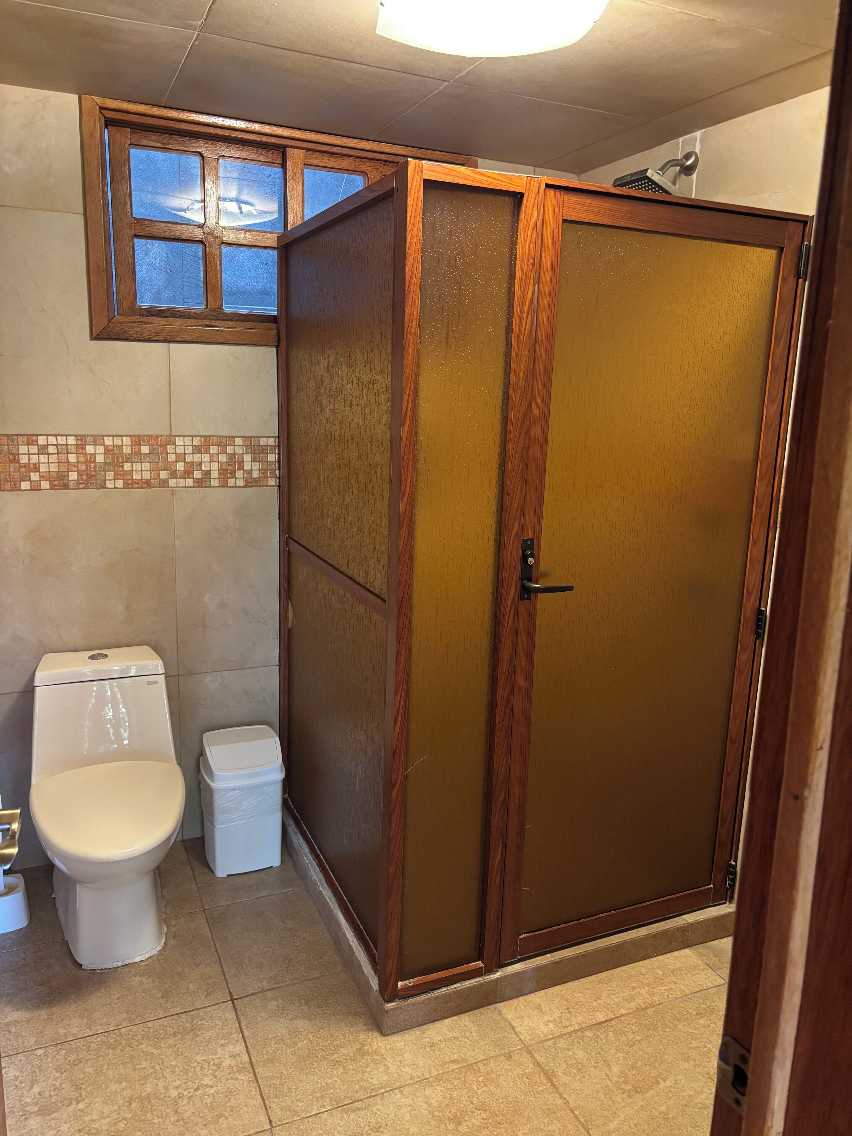 Un bagno con il water, un cestino, uno spazio doccia e una finestra.