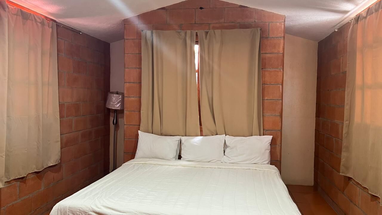 A bedroom with a brick wall, a bed with white bedding, and beige curtains.