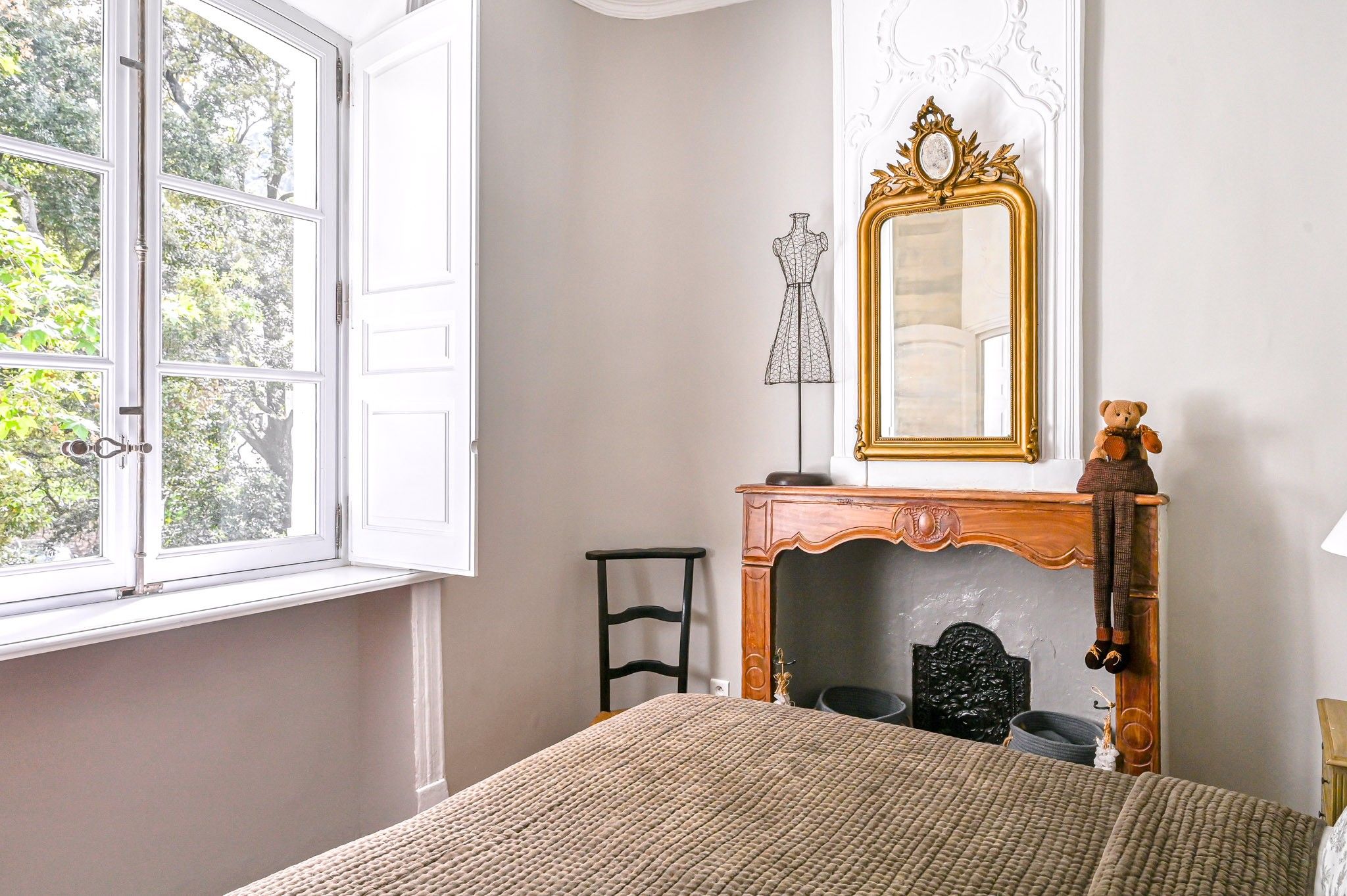 Une chambre à coucher avec un lit, une commode avec un miroir, une chaise et une fenêtre avec des rideaux.