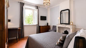 A bedroom with a bed, a dresser, a chair, a fireplace, and a large mirror.