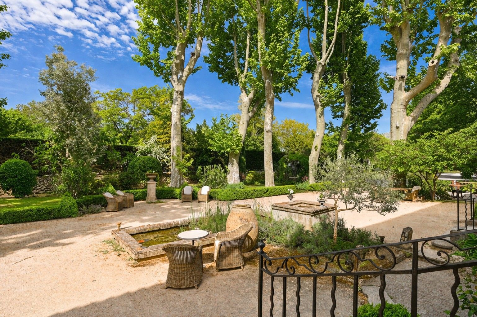 A garden with a pond, seating area, and tall trees.