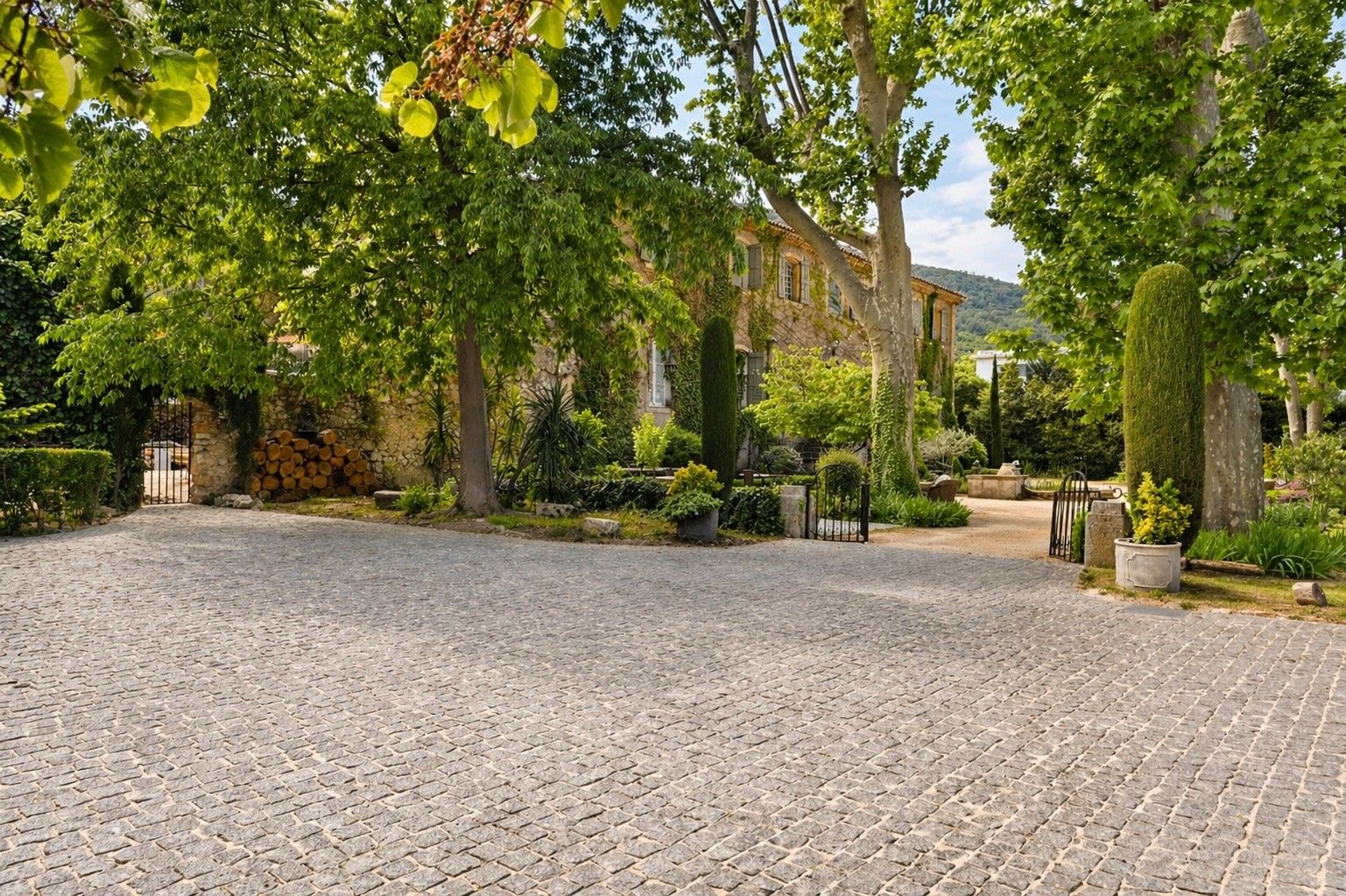Ein Kopfsteinpflasterhof mit einer Steinmauer, einem Tor und einem Gebäude mit Ziegeldach im Hintergrund.