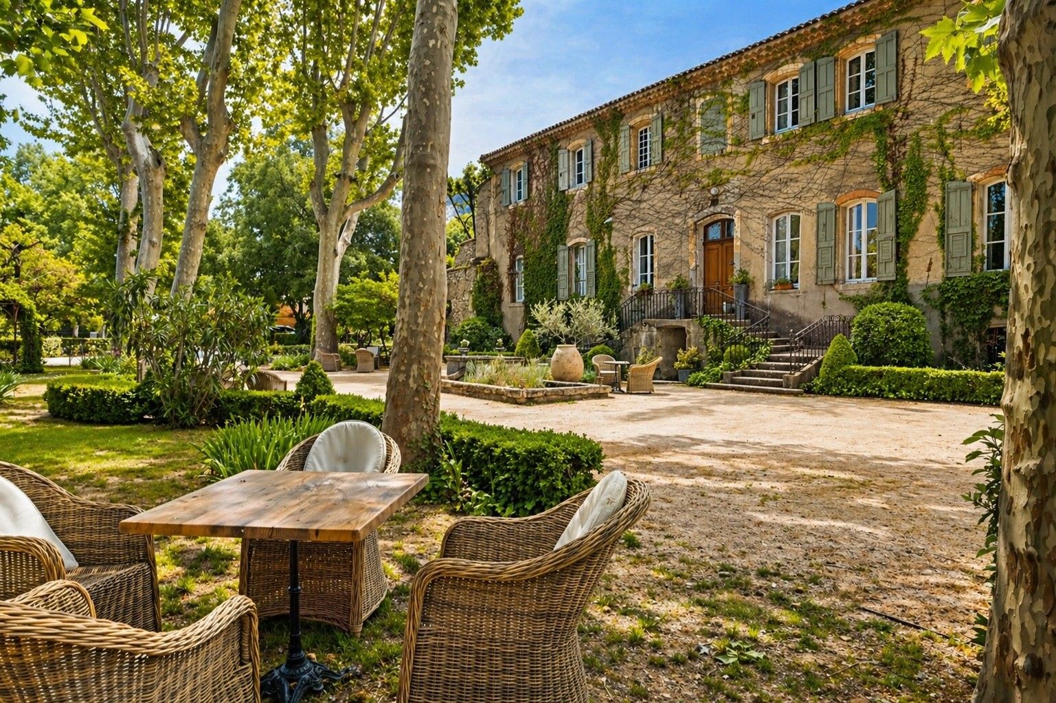 Ein Innenhof mit Sitzgelegenheiten im Freien, ein Steinhaus mit zahlreichen Fenstern und ein gepflegter Garten.