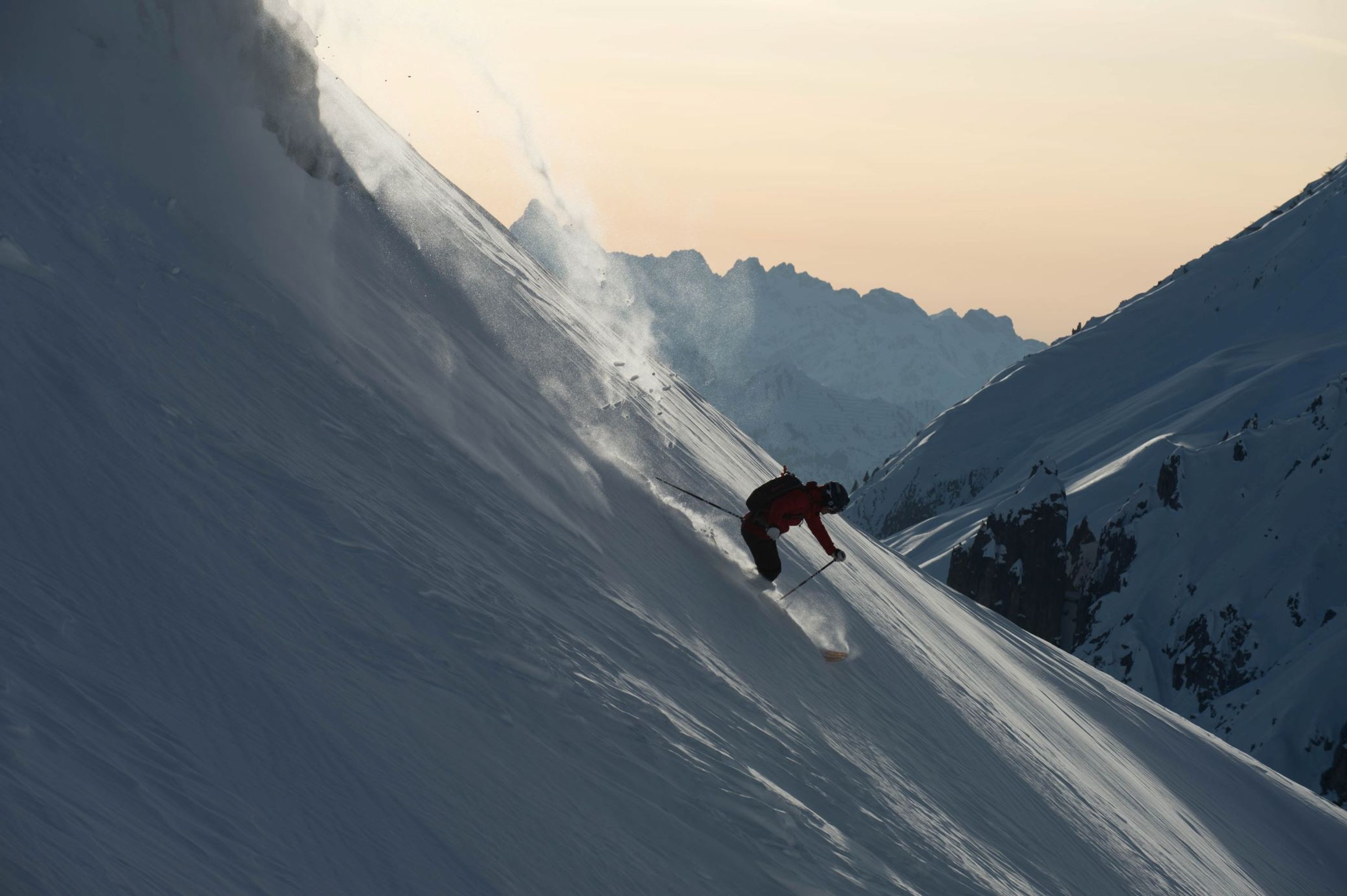 Un skieur sur une pente enneigée, avec des montagnes en arrière-plan.