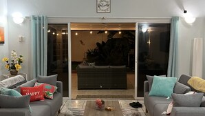 Een woonkamer met twee grijze banken, een salontafel en een vloerkleed met een patroon. Er is een schuifdeur van glas die leidt naar een buitenruimte met een bank en planten.