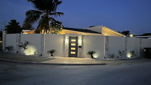 Een modern huis met een goed verlichte entree, een gevel van natuursteen en een palmboom op de achtergrond.