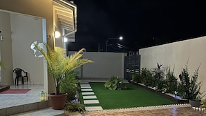 Een modern huis met een geplaveid terras, een klein gazon en een plant in een pot.