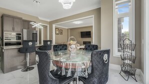 A modern kitchen with a dining area, featuring a glass table, black upholstered chairs, and a chandelier.