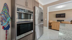 A modern kitchen with stainless steel appliances, a marble countertop, and a beige wall.