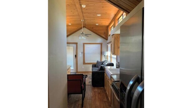 A compact kitchen with wooden flooring, a ceiling fan, and a refrigerator.