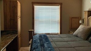 A bedroom with a sloped ceiling, a window with blinds, a bed with a patterned blanket, and wooden cabinets.