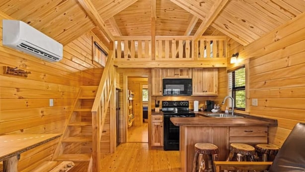A wooden cabin interior with a kitchen, dining area, and a staircase. - Barnwell Mountain Cabins #6 (Gilmer)