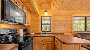 A compact kitchen with wooden cabinets, a black stove, and a sink. - Barnwell Mountain Cabins #6 (Gilmer)