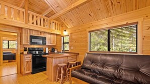 A wooden cabin interior with a kitchen, a leather sofa, and a dining area. - Barnwell Mountain Cabins #6 (Gilmer)