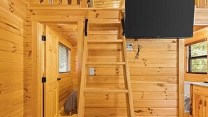 Un interior de madera con una escalera de madera, un televisor montado en la pared y ventanas con persianas.