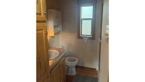 A small, compact bathroom with a wooden vanity, a toilet, and a window providing natural light. - Barnwell Mountain Cabins #8 (Gilmer)