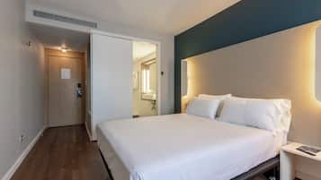 Habitación de hotel con cama, mesita de noche y baño a la vista a través de un acceso abierto.