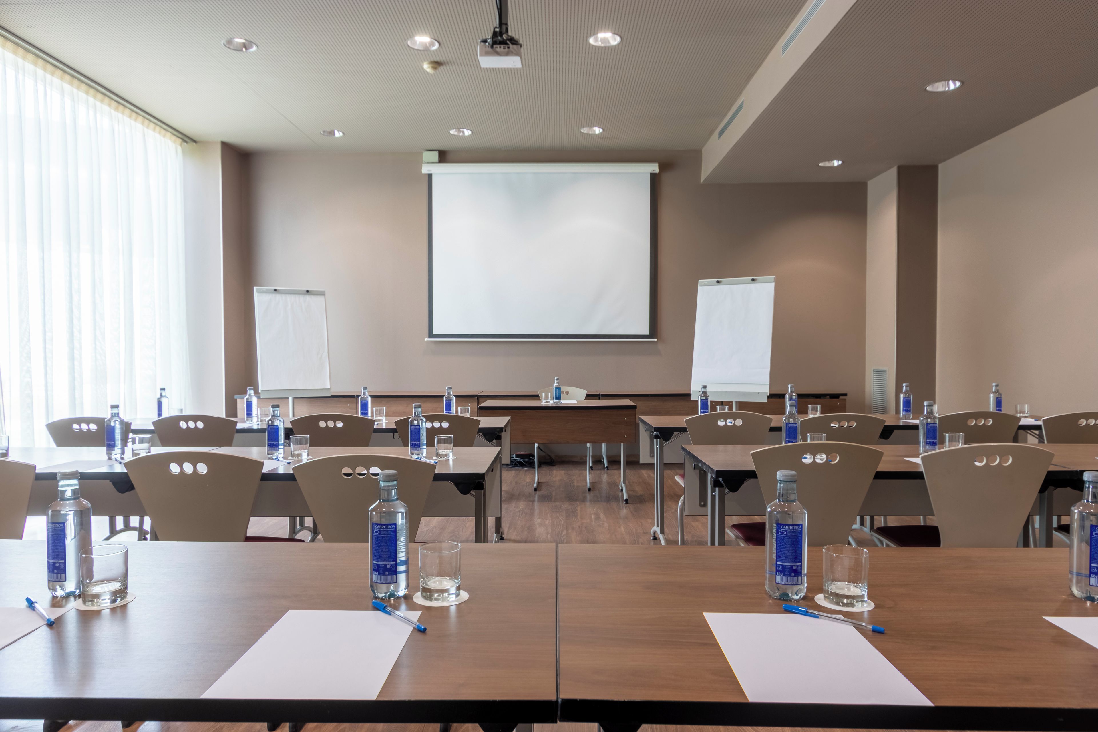 A conference room with multiple tables, chairs, water bottles, and a projector screen.