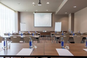 A conference room with multiple tables, chairs, water bottles, and a projector screen. - Travelodge Malaga Aeropuerto (Málaga)