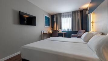 Una habitación de hotel con dos camas, un escritorio, una silla, un televisor y una ventana con cortinas.