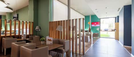 A modern hotel lobby with a wooden reception desk, seating area, and large windows.