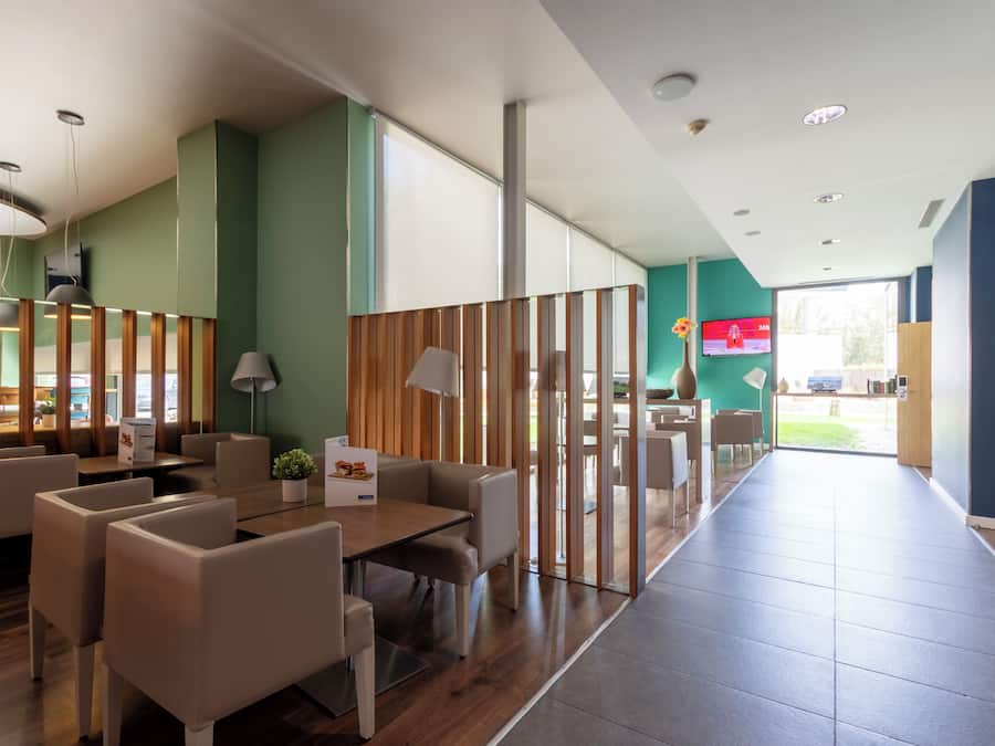 A modern hotel lobby with a wooden reception desk, seating area, and large windows.