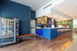 A bar area with a vending machine, blue counter, stools, and a wooden bench. - Travelodge Malaga Aeropuerto (Málaga)