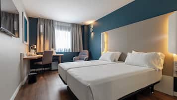 Een hotelkamer met twee bedden, een bureau met stoel, een televisie en een raam met gordijnen.