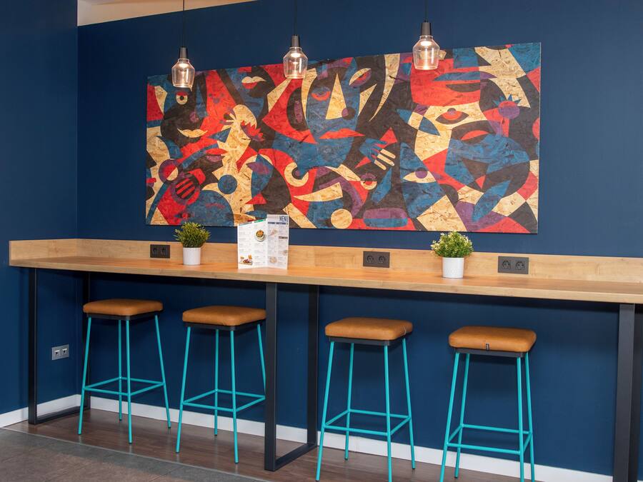 A bar area with a wooden countertop, three turquoise stools, and a colorful abstract painting on the wall.