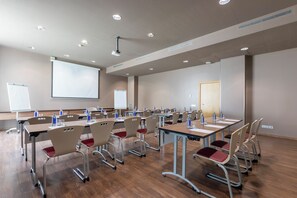 Ein Konferenzraum mit mehreren Tischen und Stühlen, einer Projektionsleinwand und einer Whiteboard.