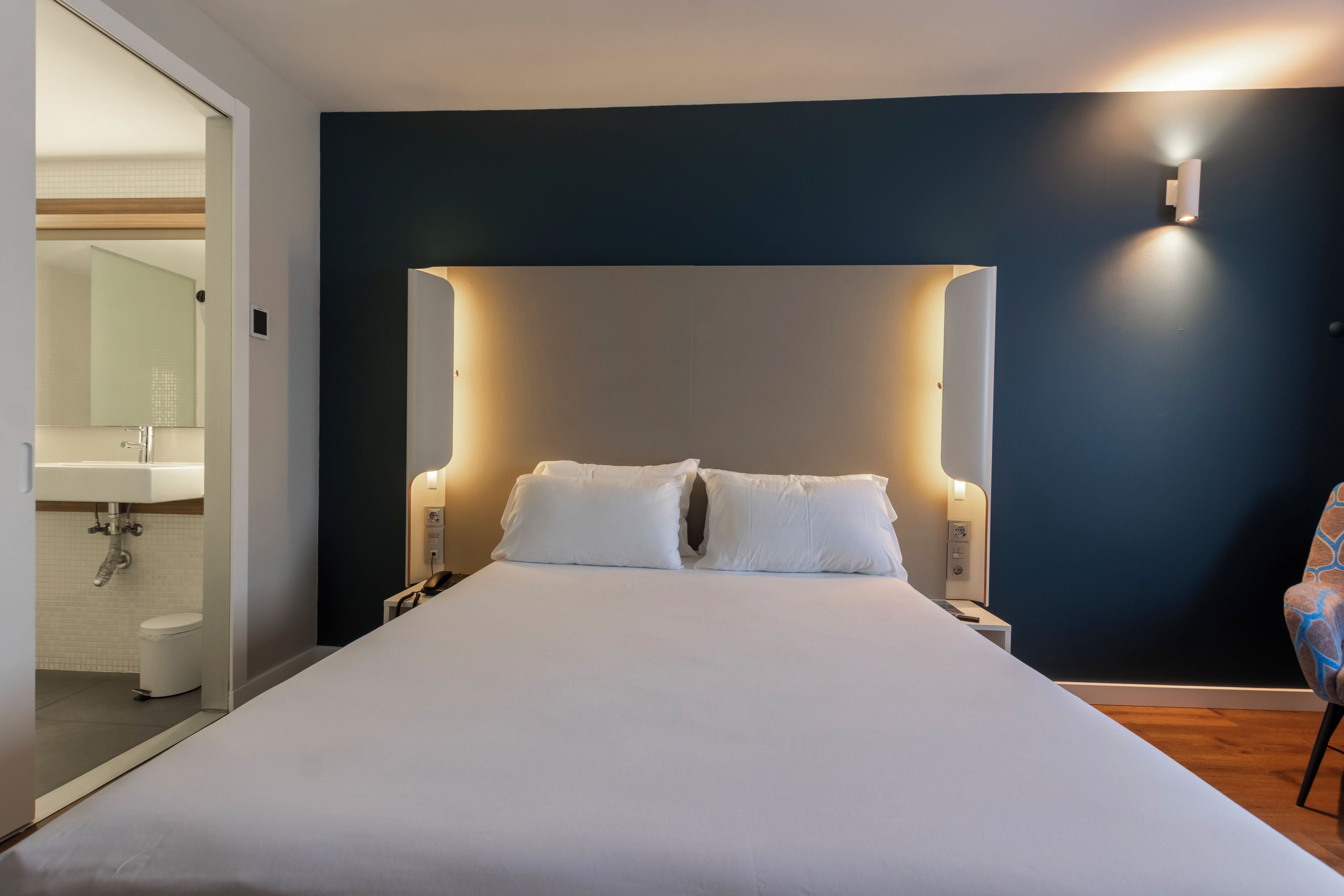 Una habitación de hotel moderna con una cama grande, una mesita de noche y una silla.