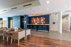 A modern hotel lobby with a bar area, seating arrangements, and a colorful abstract mural on the wall. - Travelodge Malaga Aeropuerto (Málaga)