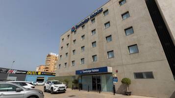 Un hotel Travelodge con fachada moderna, múltiples ventanas y un estacionamiento con automóviles.