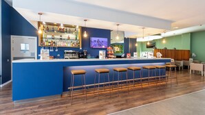 Un espace bar avec un comptoir bleu, de nombreux tabourets et une variété de bouteilles et de verres.