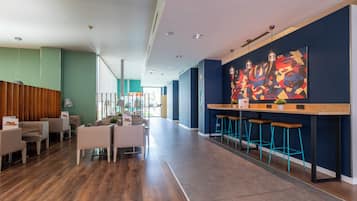 Eine moderne Hotelhalle mit einem Holzerrezeptionstresen, Barhocker und einem farbenfrohen, abstrakten Gemälde an der Wand.