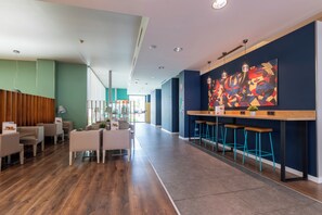 A modern hotel lobby with a wooden reception desk, bar stools, and a colorful abstract painting on the wall. - Travelodge Malaga Aeropuerto (Málaga)